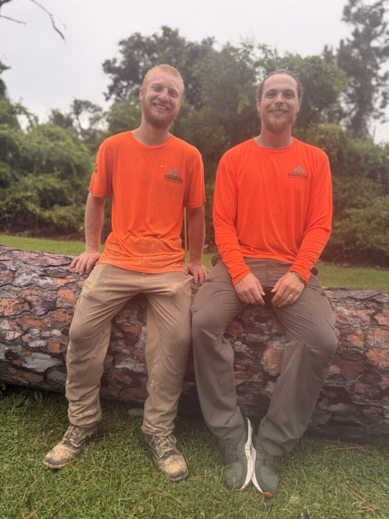 Two Cornerstone Property Services crew members sitting on a felled pine log after finishing a tree removal in Northwest Florida